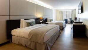 A hotel room with two beds, a desk, a chair, a flat-screen TV, and a large window with curtains. - Oro Verde Cuenca (Cuenca)