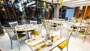 A restaurant with white and green chairs, neatly set tables with cutlery, and hanging plants.