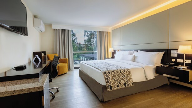 A hotel room with a bed, desk, chair, and a view of the outdoors.