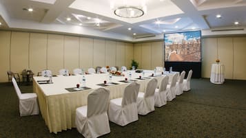 A conference room with a long table, chairs, and a projector screen displaying a building.