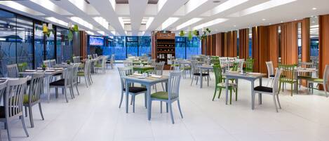 A modern dining area with multiple tables and chairs, a television screen, and a display case with items.