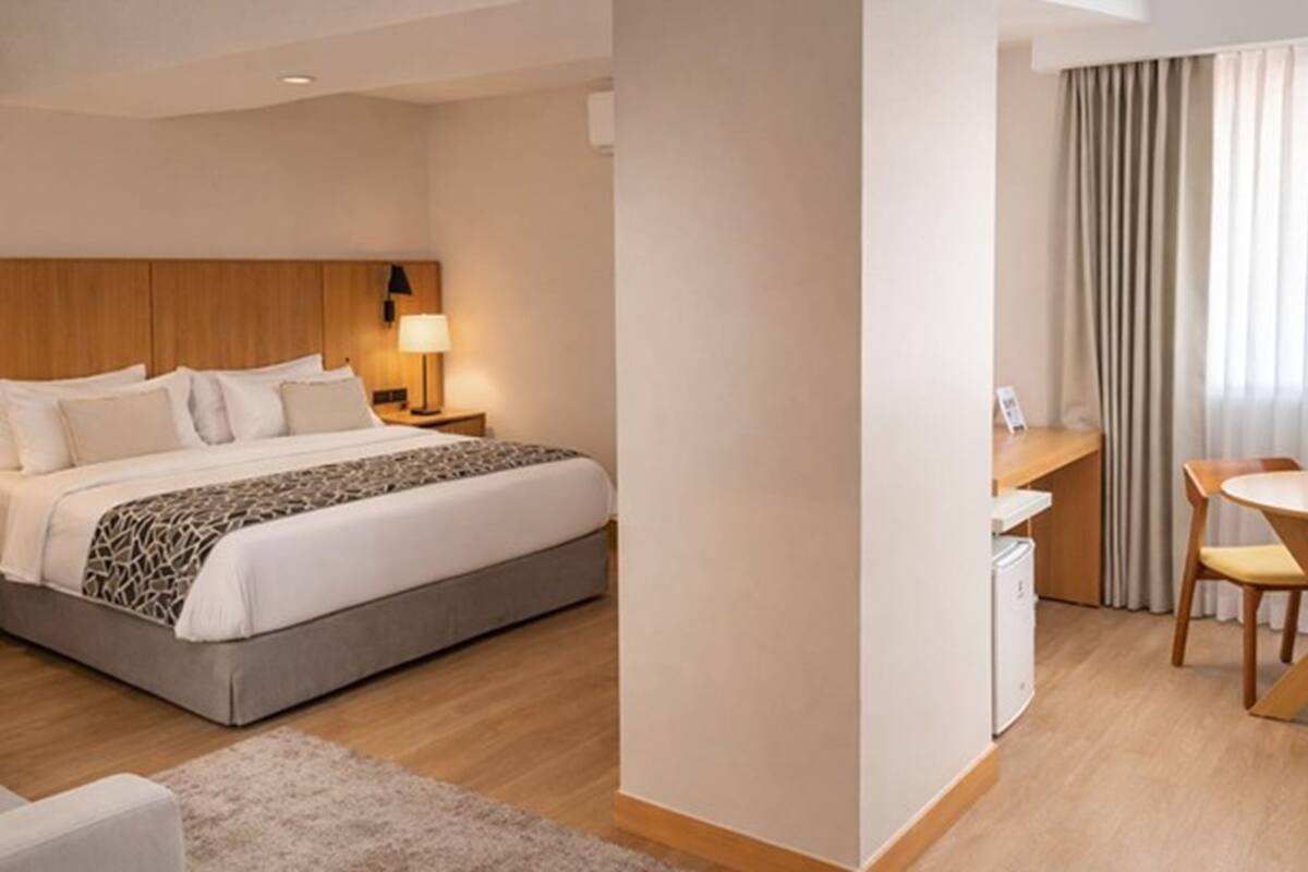 A hotel room with a bed, bedside table, lamp, desk, chair, and curtains.