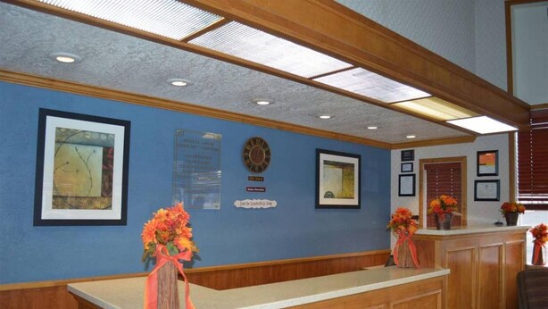A reception area with a wooden reception desk, framed artwork on the walls, a clock, and flower arrangements. - Holiday Motel (Winnemucca)