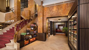 A grand lobby with marble floors, a staircase with red carpet, and a wine and snack display. - NH Atlanta Rotterdam (Rotterdam)