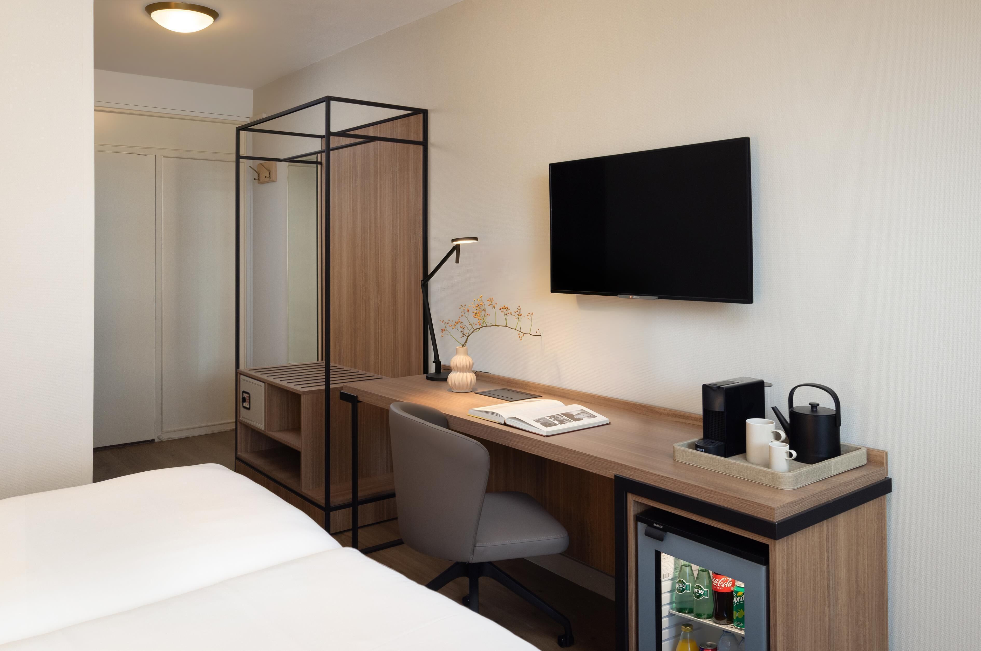 Una camera d'albergo con una scrivania in legno, una sedia, una televisione, una libreria e un frigobar.