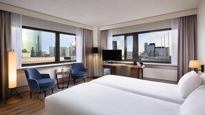 A hotel room with a large bed, two armchairs, a desk with a flat-screen TV, and a city view. - NH Atlanta Rotterdam (Rotterdam)