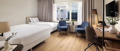 A hotel room with two beds, a desk, a chair, a TV, and a window with curtains.
