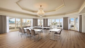 A spacious conference room with a large chandelier, multiple tables, and chairs, large windows with city views. - NH Atlanta Rotterdam (Rotterdam)