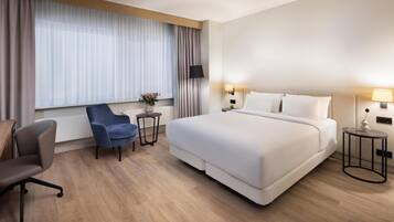 A hotel room with a large bed, a desk, a chair, and a window with curtains.
