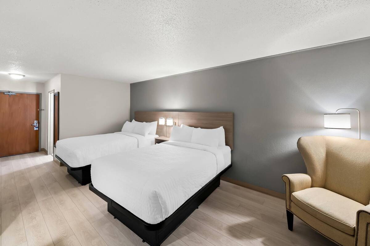 A hotel room with two beds, a chair, and a nightstand.