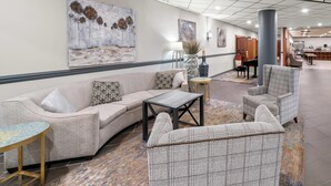 A lobby with a sofa, armchairs, a coffee table, a lamp, and artwork on the walls. - Clarion Inn and Suites Convention Center Kearney (Kearney)