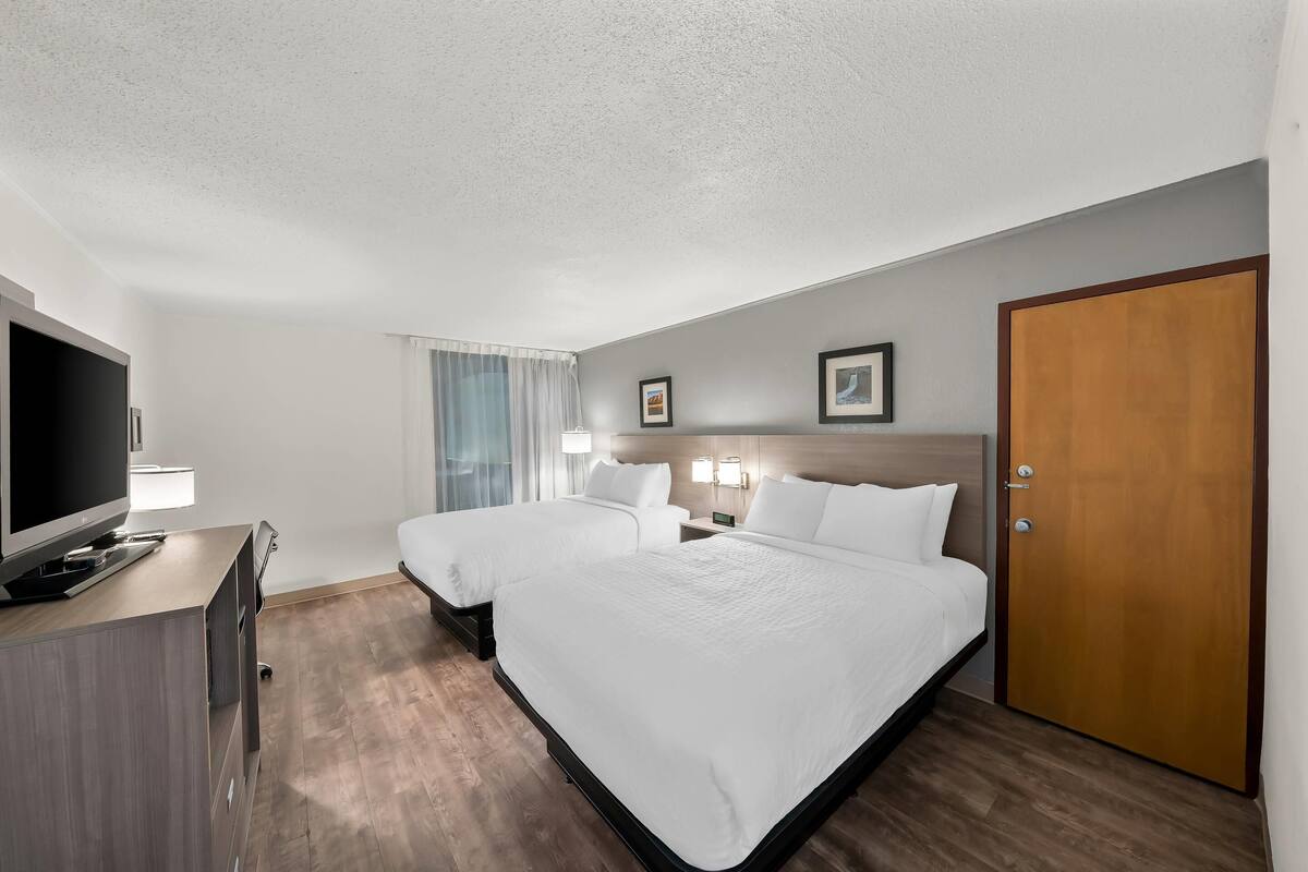 A hotel room with two beds, a TV, a desk, and a door.