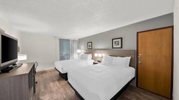 A hotel room with two beds, a TV, a desk, and a door.