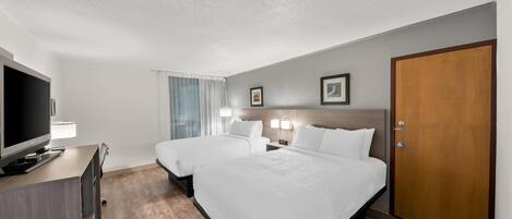A hotel room with two beds, a TV, a desk, and a door.