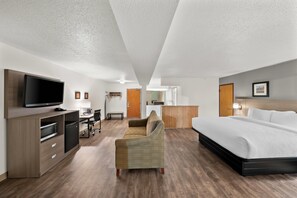 A hotel room with a bed, a TV, a desk, a chair, and a kitchenette. - Clarion Inn and Suites Convention Center Kearney (Kearney)