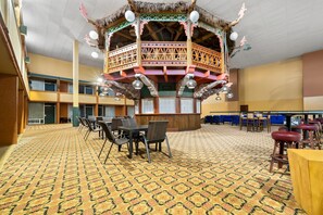 A spacious lobby with a patterned carpet, a central seating area with tables and chairs, and a decorative thatched structure. - Clarion Inn and Suites Convention Center Kearney (Kearney)