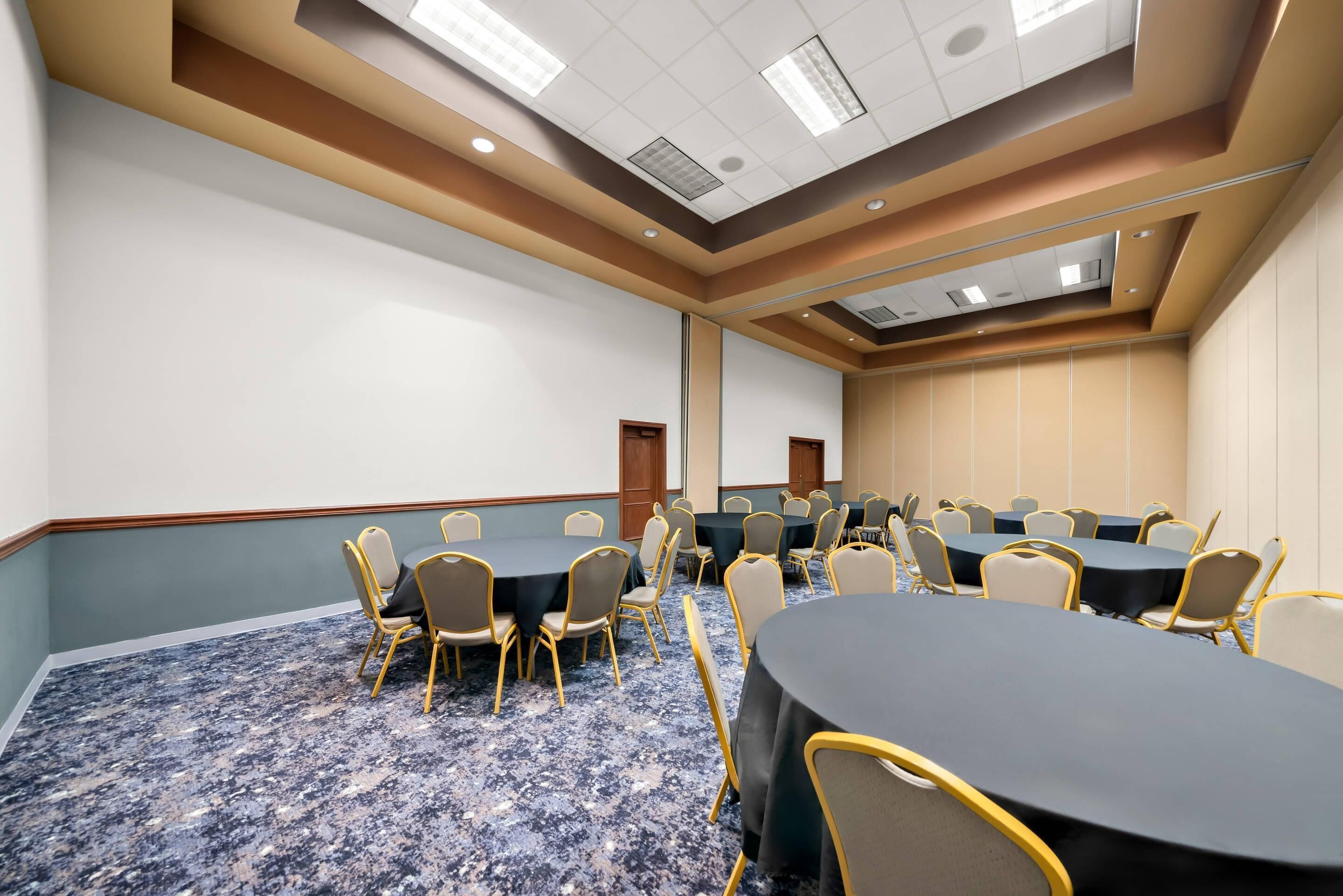 Un salón de conferencias con mesas redondas, sillas y suelo alfombrado.