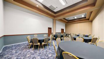 A conference room with round tables, chairs, and a carpeted floor.