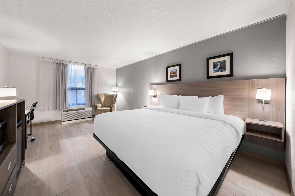A hotel room with a large bed, a desk, a chair, a desk lamp, and a window with curtains.