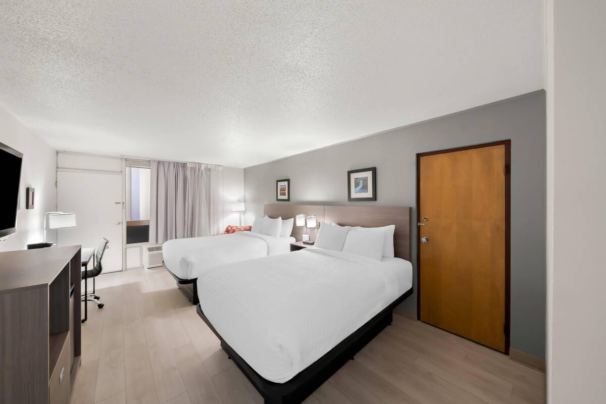 A hotel room with two beds, a desk, a chair, a TV, and a door.