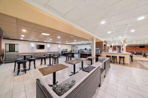 A spacious indoor area with multiple seating options including tables and bar stools, a kitchen area, and a television mounted on the wall. - Clarion Inn and Suites Convention Center Kearney (Kearney)