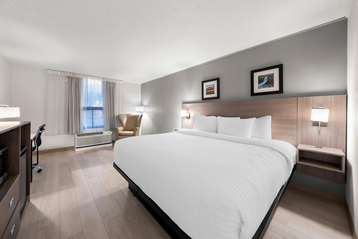A hotel room with a large bed, bedside tables, a desk with a chair, a window with curtains, and wall-mounted lamps.