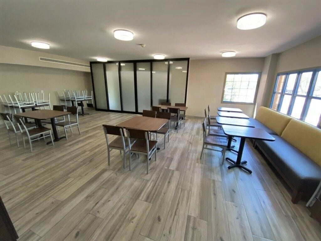 A spacious room with multiple tables and chairs, a sofa, and large windows providing natural light.