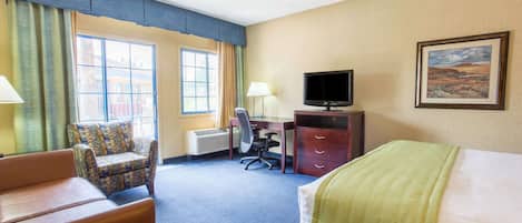 A hotel room with a bed, a desk with a computer, a chair, and a television.