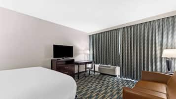 Habitación de hotel con cama, escritorio, silla, televisor y ventana con cortinas.