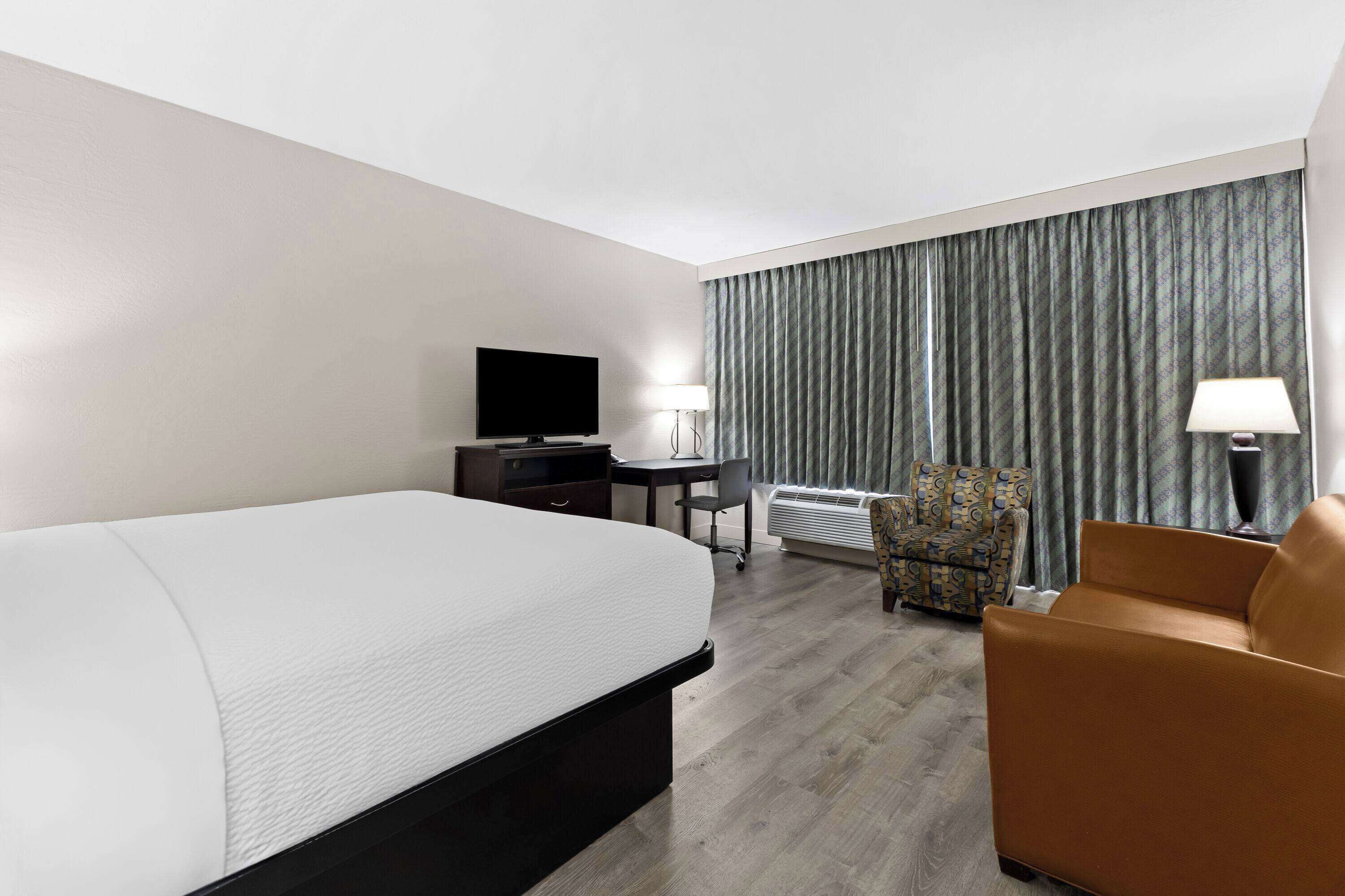 Habitación de hotel con cama, escritorio, silla, televisor y ventana con cortinas.