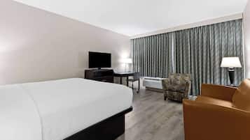 Habitación de hotel con cama, escritorio, silla, televisor y ventana con cortinas.