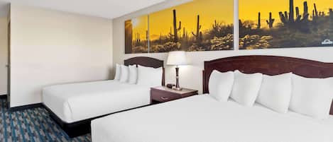 Habitación de hotel con dos camas, una mesita de noche con lámpara y un cuadro con temática desértica.