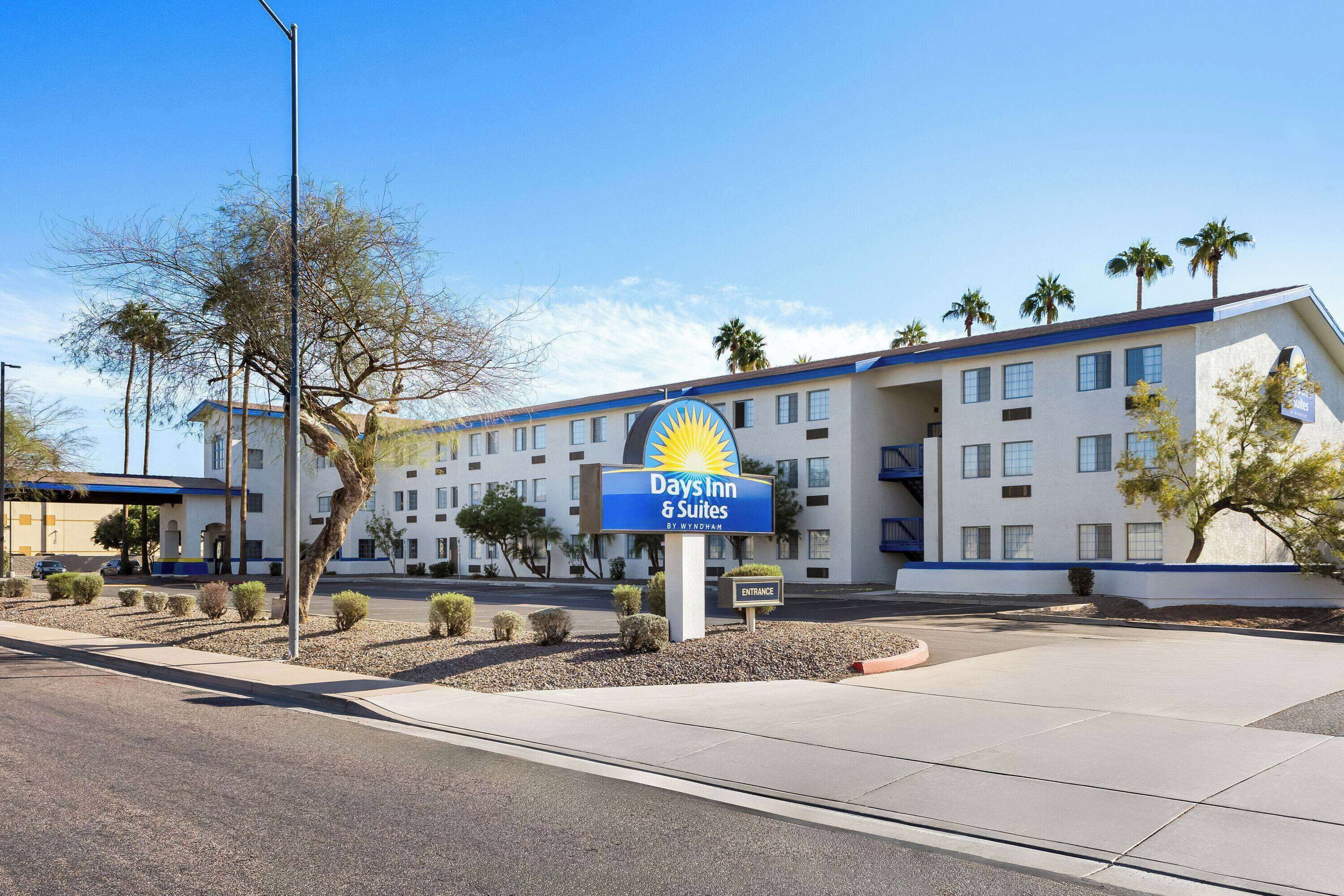 A Days Inn & Suites building with a clear sky, palm trees, and a parking lot.