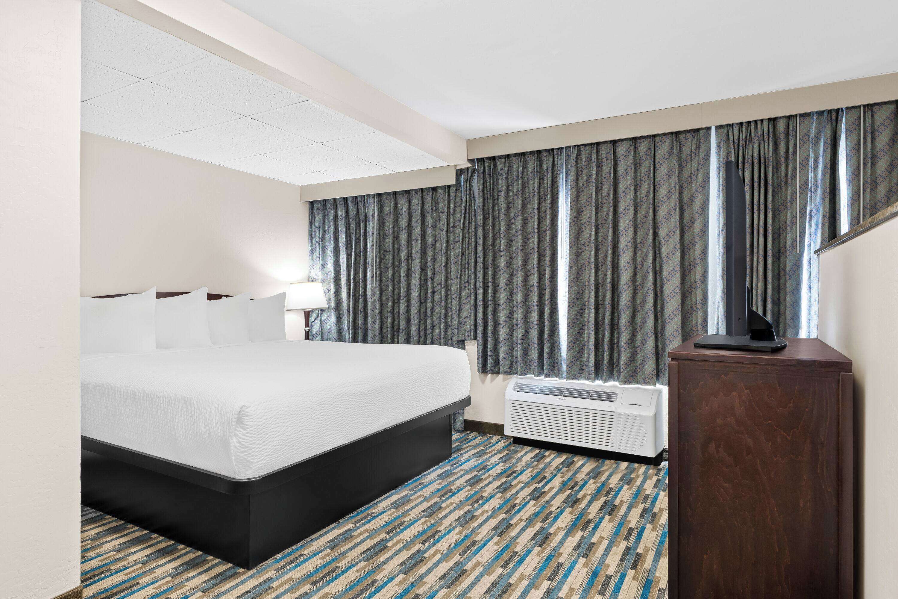 Ein Hotelzimmer mit Bett, Schreibtisch, Lampe und einem Fenster mit Vorhängen.