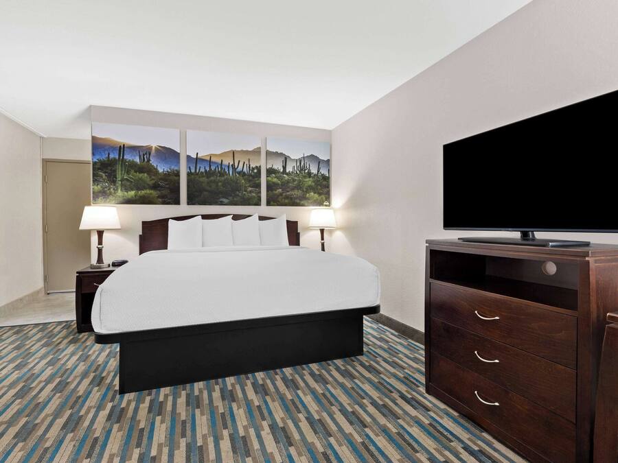 Habitación de hotel con cama, televisión, cómoda y dos lámparas de pared.