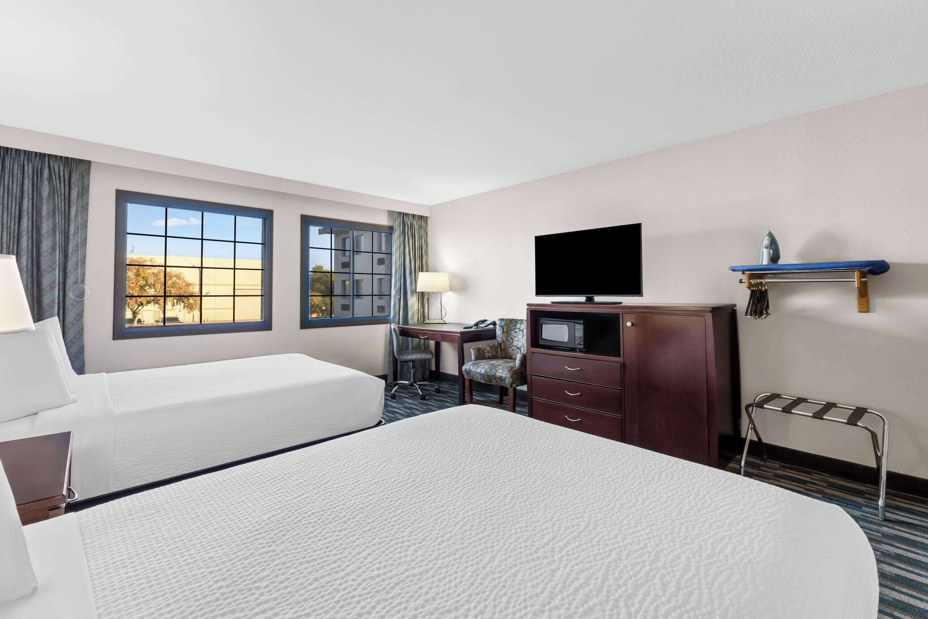 A hotel room with two beds, a desk with a computer, a TV, and a small ironing board.