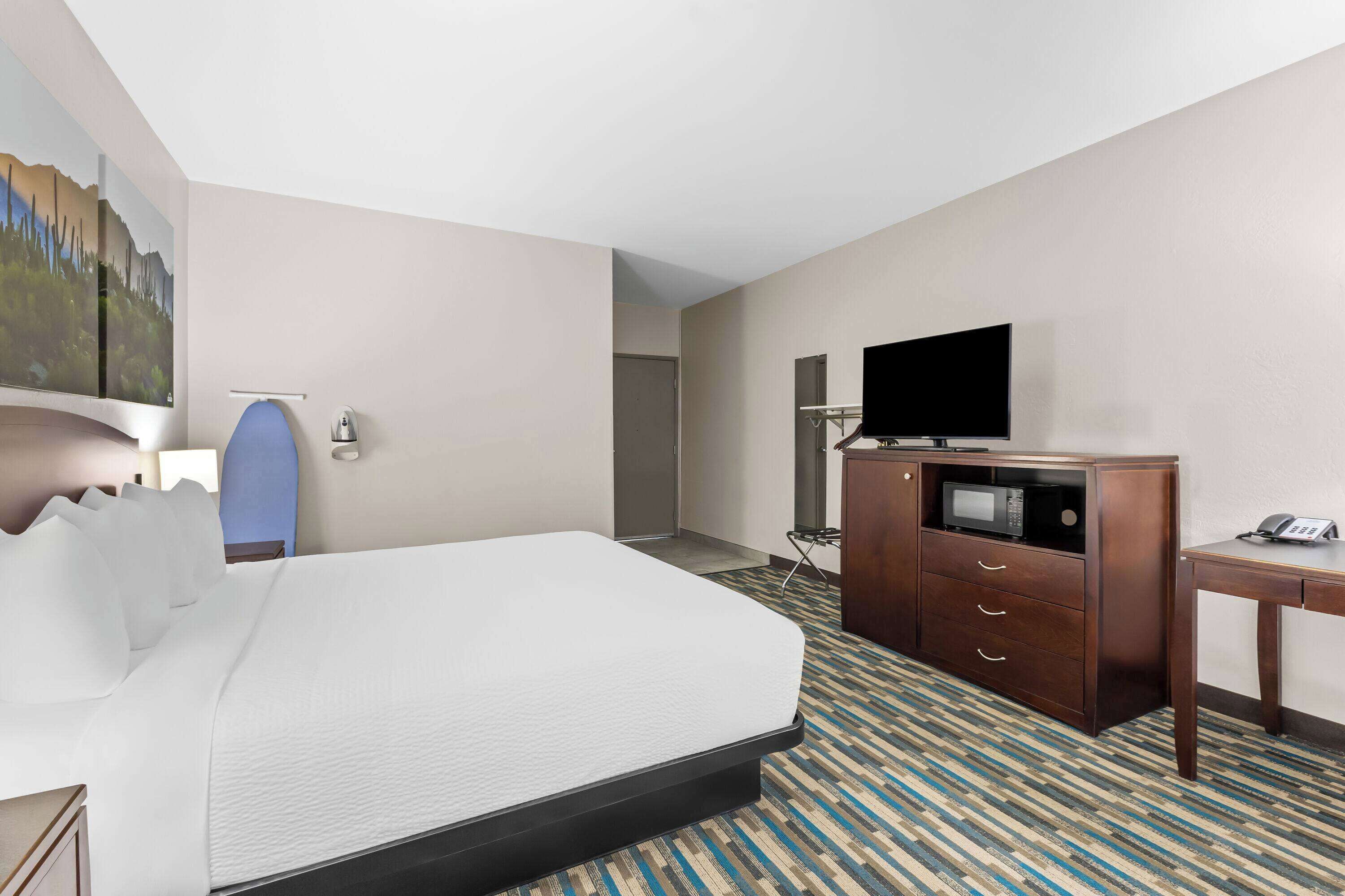 A hotel room with a bed, a desk, a television, a microwave, and a cabinet.