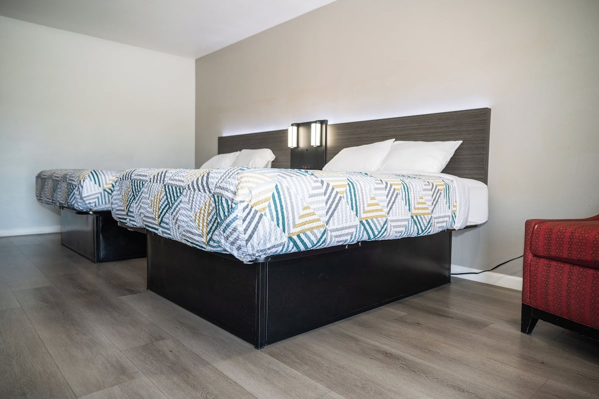 A double bed with a patterned bedspread, a bedside table with a lamp, and a red chair.