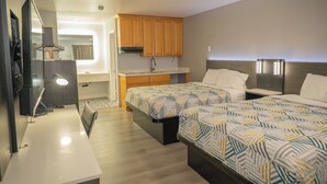 A compact hotel room with two beds, a kitchenette, a mirror, and a TV.