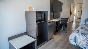 Une chambre d’hôtel de taille réduite, équipée d’une kitchenette, d’un bureau, d’une chaise et d’un lit.