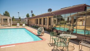 Une piscine dotée d’une terrasse carrelée, entourée de chaises longues et de tables, et un bâtiment aux grandes fenêtres qui reflètent l’image de la piscine.