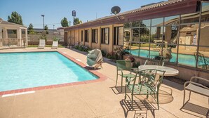 A swimming pool with a patio area, outdoor seating, and a view of a poolside area with lounge chairs and a dining table.