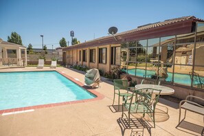 A swimming pool with a patio area, outdoor seating, and a view of a poolside area with lounge chairs and a dining table.