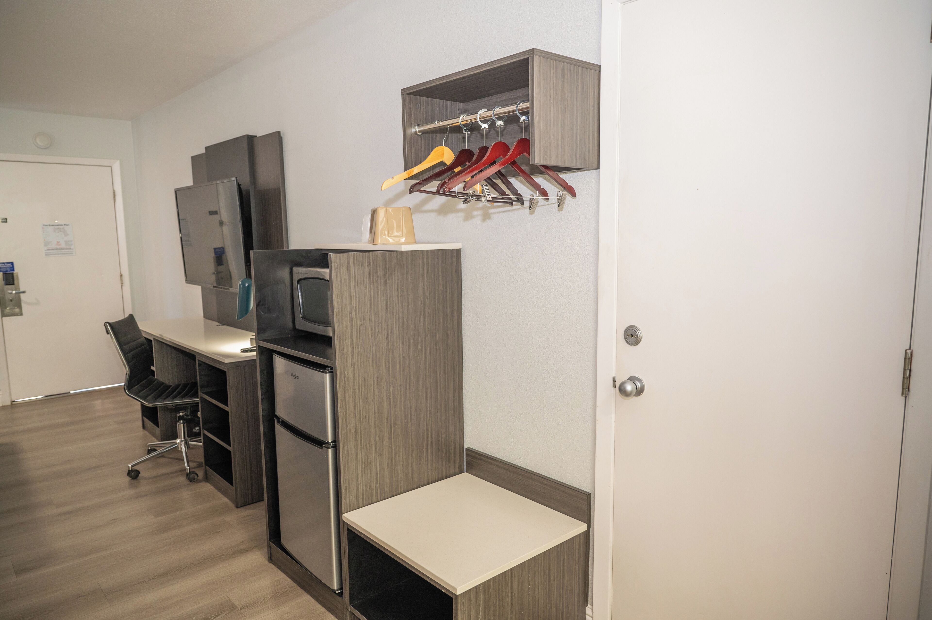 A compact hotel room with a kitchenette, a desk, and a coat rack.