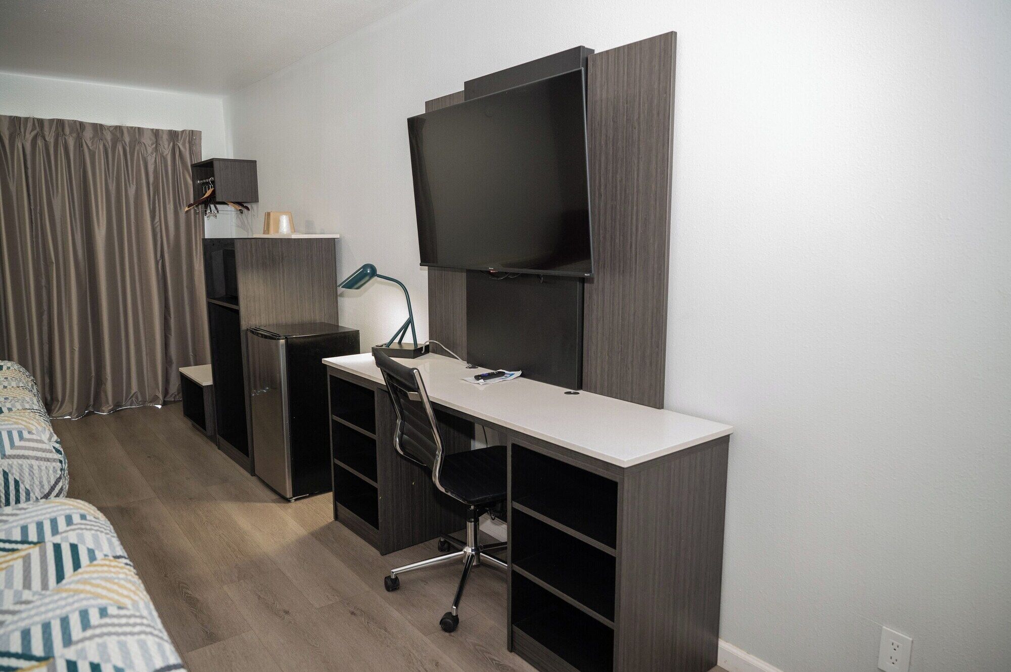 Habitación de hotel compacta con cama, escritorio con silla, televisor y armario.