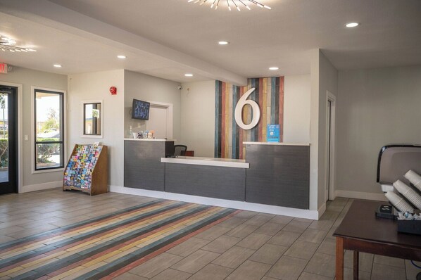A reception area with a modern design, including a reception desk, a large number '6' sign, a flat-screen TV, and a colorful striped rug.
