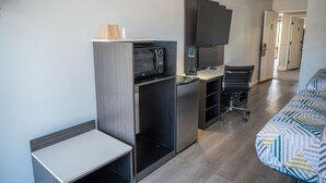 Une chambre d’hôtel compacte comprenant un coin cuisine, un lit avec une literie à motifs, un bureau avec une chaise et un téléviseur à écran plat.