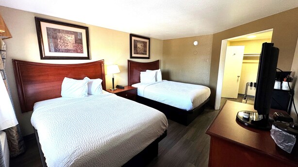 A hotel room with two beds, a desk with a lamp, and a TV.
