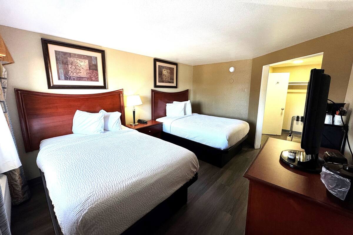 A hotel room with two beds, a desk with a lamp, and a TV.