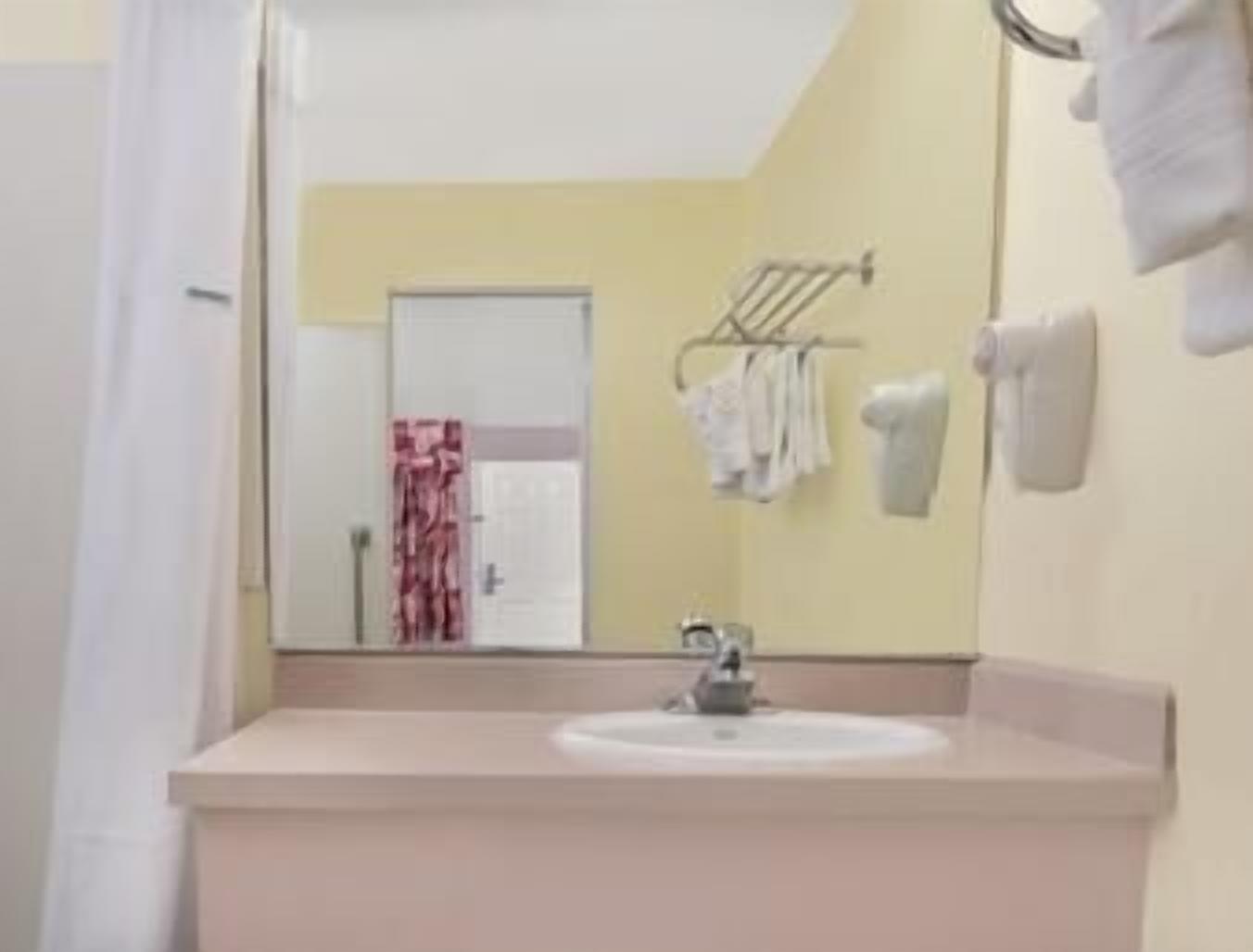 Un baño con lavabo, espejo, toallero y una puerta que da a otra habitación.